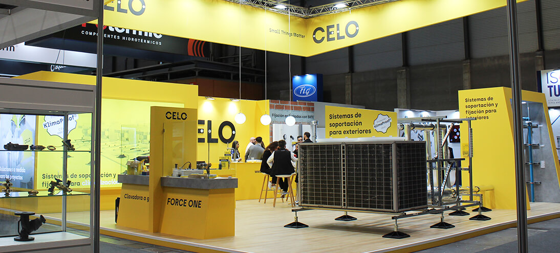 Stand de CELO en la feria C&R con estructura y mostradores amarillos y expositores de productos de fijación y suportación